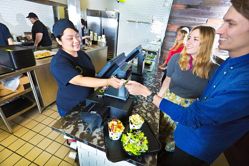 Wait staff and kitchen staff working and serving customers over the counter in a fast food restaurant.