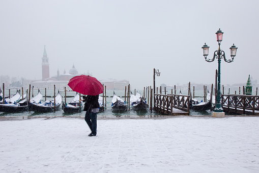 Venice, Italy - March 1, 2018: Venice in snow, woman with red umbrella, Riva degli Schiavoni, with gondolas on Grand Channel, St. Mark square, snowing in Venice, Italy, march 2018