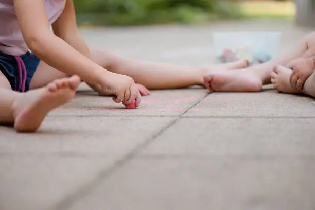 Crop of little children drawing with chalk on paving outdoors in backyard