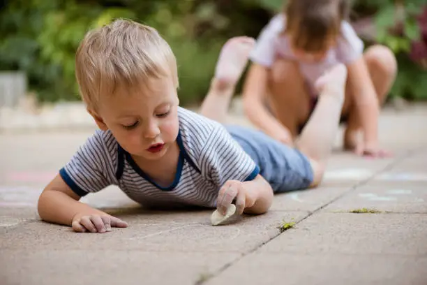 Children drawing together drawing with chalk outdoor on paving - boy in front