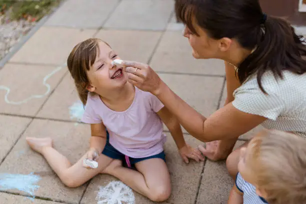Having fun together - mother is drawing with chalk on nose of her daughter in backyard