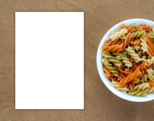 istock Multicolor spiral macaroni pasta in a white bowl on a brown rustic background texture with a side. Close-up with the top. White space for text and ideas. 945729440