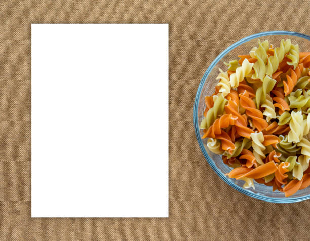 istock Multicolor spiral macaroni Pasta in a glass cup on a brown suburban background texture with a side. Close-up with the top. White space for text and ideas. 945730062