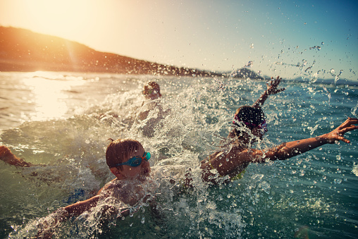 Brothers and sister are having fun in sea waves. Kids are jumping into incoming waves and laughing.
Sunny summer day evening.
Nikon D800