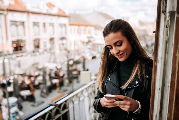 istock Young woman using phone while standing on a terrace over the city street. 945747700