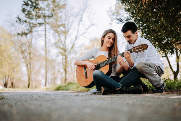 istock Guy teaching girl how to play guitar at the park. 945747820