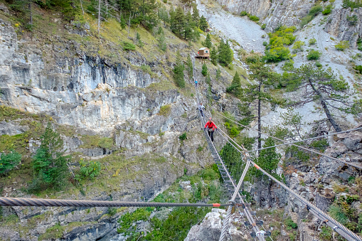 People walking on the suspension bridge winding through the Gorge di San Gervasio above the stream Piccola Dora. It is located in Val di Susa, Piedmont, northern Italy
