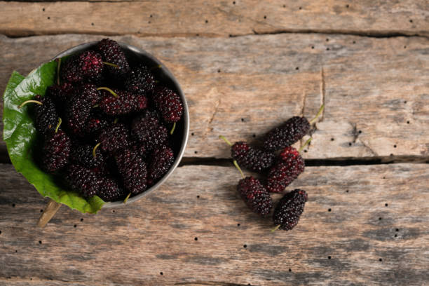 Fresh black mulberry in a rustic bowl on a wood background