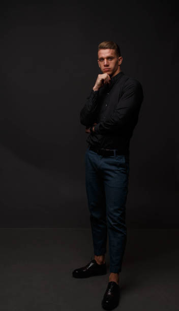atrakcyjny biały mężczyzna w czarnej koszuli i niebieskich spodniach stoi na ciemnym tle - funky men business human arm zdjęcia i obrazy z banku zdjęć