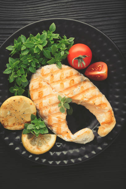 istock Grilled salmon with lemon and basil on dark background. Top view 945820136
