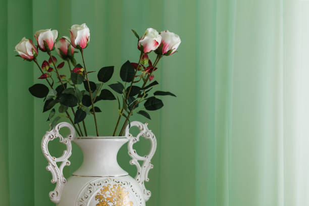 Beautiful bouquet of pink lisianthus flowers  put in a rustic looking tea pot as a vase, that is standing on a book that's on a retro white chair.