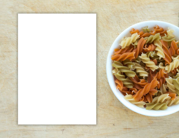 istock Multicolor spiral macaroni pasta in a white bowl on a wooden table textured background with a side. Close-up with the top. White space for text and ideas. 945837280