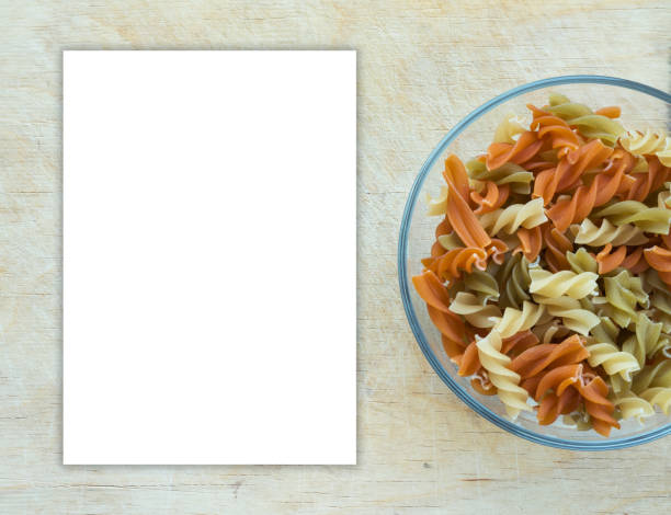 istock Multicolor spiral macaroni Pasta in a glass cup on a wooden table textured background with a side. Close-up with the top. White space for text and ideas. 945837632