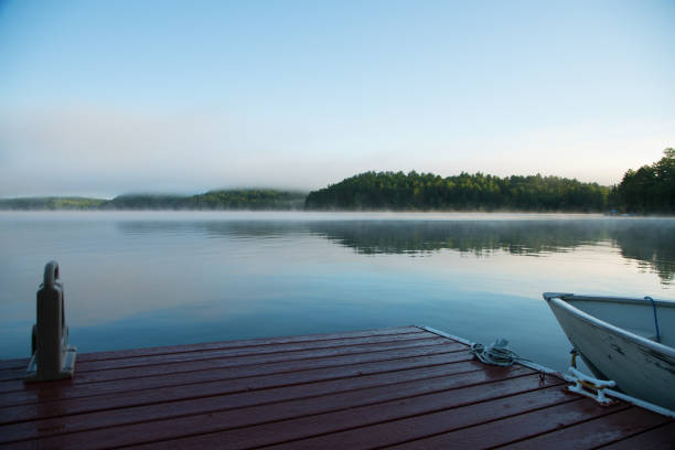 Sunrise reflection over St-Maurice river and a pier during summer in Shawinigan.Branches are in foreground,