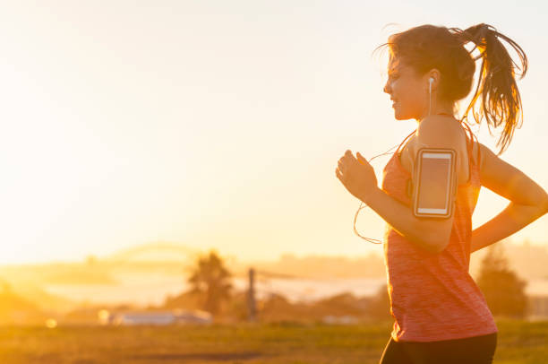 Woman running with mobile phone on her arm. Woman running with mobile phone on her arm. She is exercising at sunset or sunrise with the city of Sydney in the background. She has a smart phone on her arm and is listening to music. Copy space. She is smiling and happy. sports training australia stock pictures, royalty-free photos & images