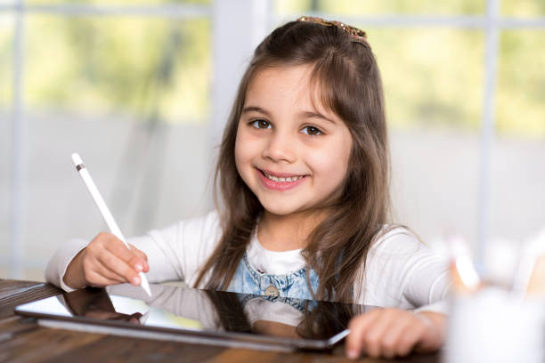 istock Little Girl Drawing Digital Picture On Electronic Touch Pad With Bluetooth Pen 945882164