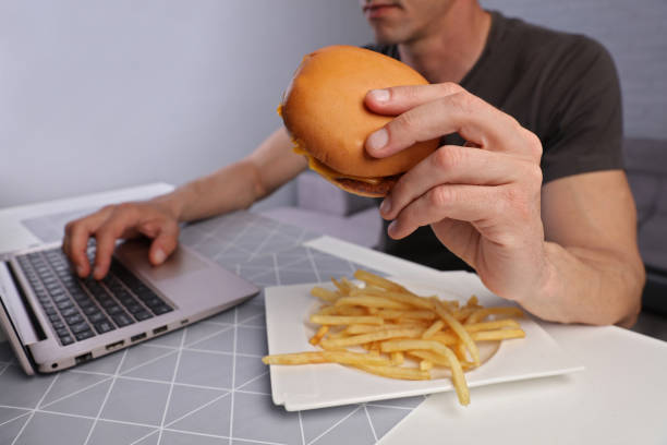 überarbeitete business mann isst hamburger / junk food für diner. ungesunde ernährung führt zu chronischer gastritis oder ulcus - eating sandwich emotional stress food stock-fotos und bilder