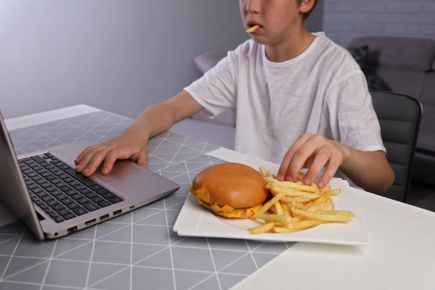 dzieci złe nawyki żywieniowe, dziecko jedzenie niezdrowego fast foodów i granie w gry komputerowe - overweight child eating hamburger zdjęcia i obrazy z banku zdjęć