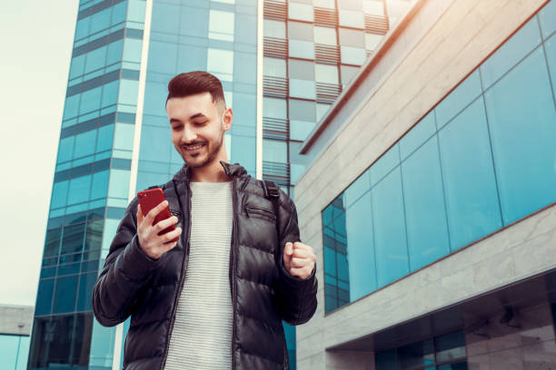 istock Arabian student using smartphone outside. Successful young man. Excited guy looks at phone in front of modern building 945889304