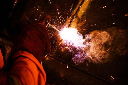 Welding in action as a man goes about connecting two pieces of metal.