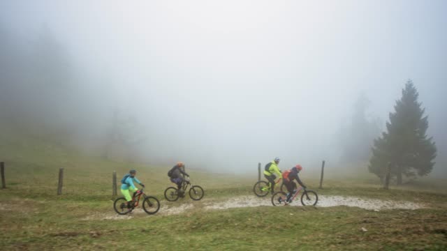 Four mountain bikers riding down a mountain trail in heavy fog