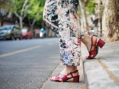 Close up on girl's feet wearing red sandals in the city, urban road background.