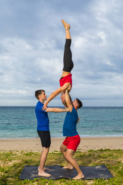акробатическая йога двое мужчин, держащих перевернутую даму - yoga challenge for 3 стоковые фото и изображения