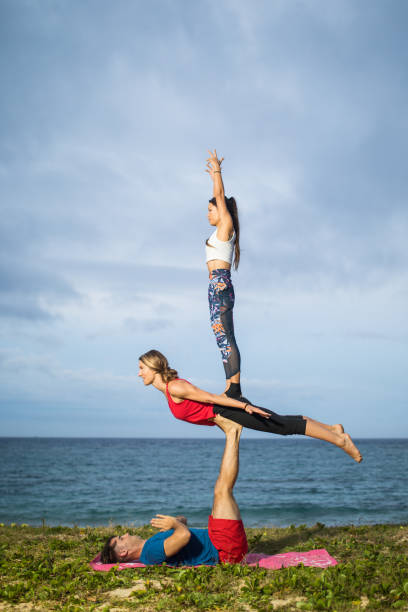 расширенная акробатическая йога на пляже - yoga challenge for 3 стоковые фото и изображения