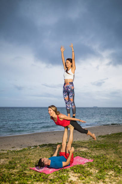 расширенная акробатическая йога на пляже - yoga challenge for 3 стоковые фото и изображения