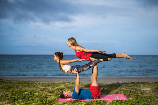расширенная акробатическая йога на пляже - yoga challenge for 3 стоковые фото и изображения