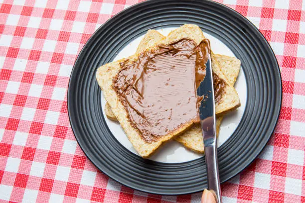 Closeup of an unknown woman spreading chocolate cream on a slice of bread with a knife
