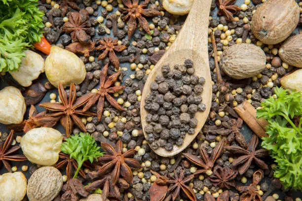 Top view of various herbs and spices with black peppercorn in the wooden spoon