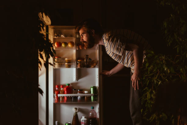 man looking for snacks in the refrigerator late night - lanchar imagens e fotografias de stock