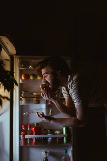 istock Man eating in front of the refrigerator late night 945954156