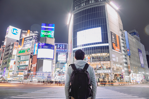 An asian male tourist standing on Shibuya crossing and looking up, where is the world famous busy crossing in Japan.