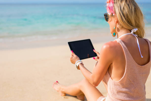 istock Young woman holding tablet on the beach 945960774