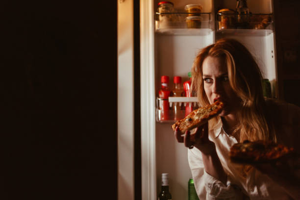 istock Young woman eating pizza late night 945964388