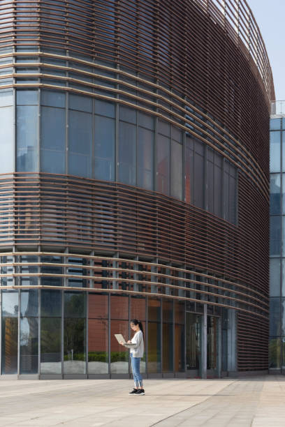 young woman using laptop front of office building,China.