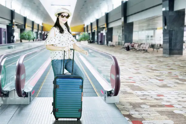 Caucasian woman wearing sunglasses while standing in the airport hall with a luggage
