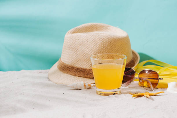istock Summer background. Beach accessories flip flops; sunglasses; hat and orange juice on sand background 945975400