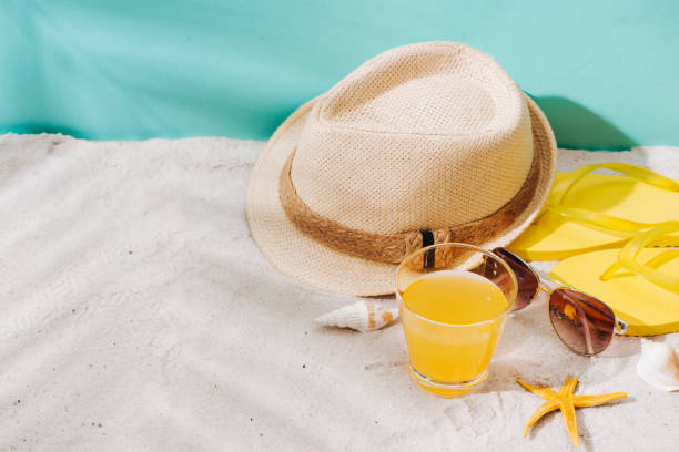 istock Summer background. Beach accessories flip flops, sunglasses, hat and orange juice on sand background 945975510