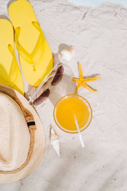 istock Summer background. Beach accessories flip flops, sunglasses, hat and orange juice on sand background 945975536