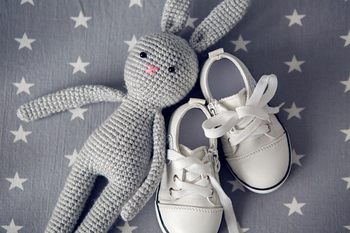 grey knitted toy rabbit, and children's white shoes are on grey background with stars