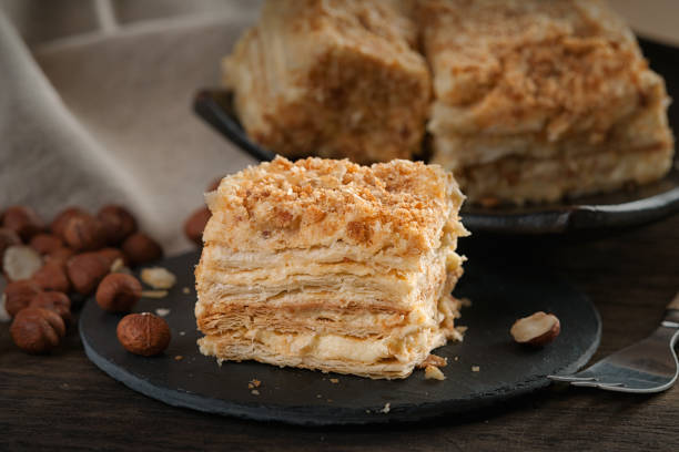 istock Slices of sweet classic layered cake Napoleon, fork and hazelnuts 945989980