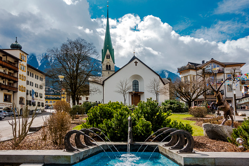 Mayrhofen, Austria - April 05, 2018: Church and fountain in center of Mayrhofen in Zillertal. Around are many restaurants, hotels and shops.