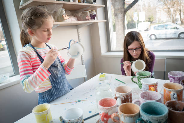 istock Girls painting pottery cups 945996136