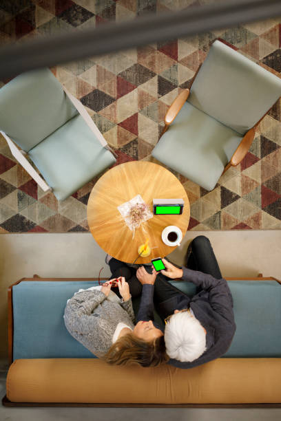 istock Senior couple sitting in retro hotel drink coffee and chatting. Active seniors, using digital tablet and smartphone, browsing the internet.  Directly above. 945996818
