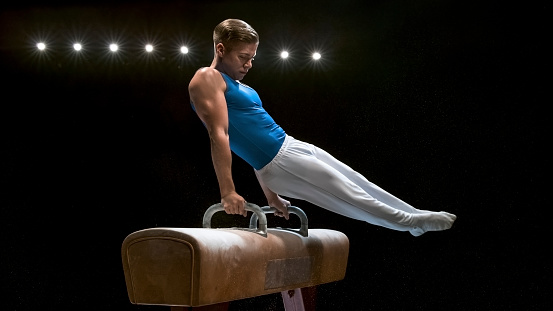 Young male gymnast performing on pommel horse.