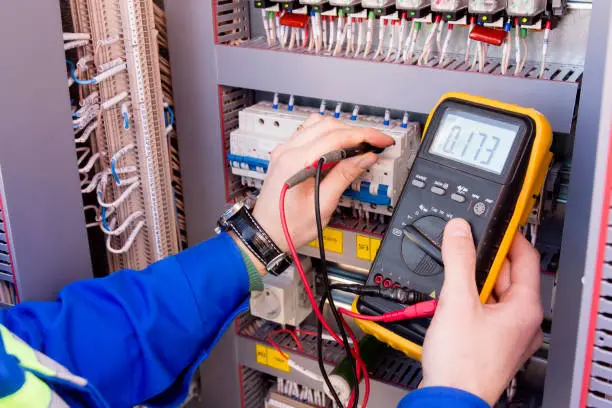multimeter is in hands of engineer in electrical cabinet. Adjustment of automated control system for industrial equipment control cabinets. electrician measures voltage by tester