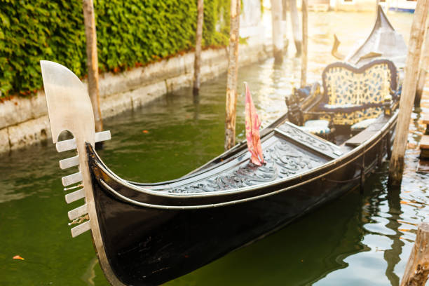 one of famous venetian gondolas laid up at its moorings against a cityscape with red house and bridge - venice italy veneto architecture blue imagens e fotografias de stock